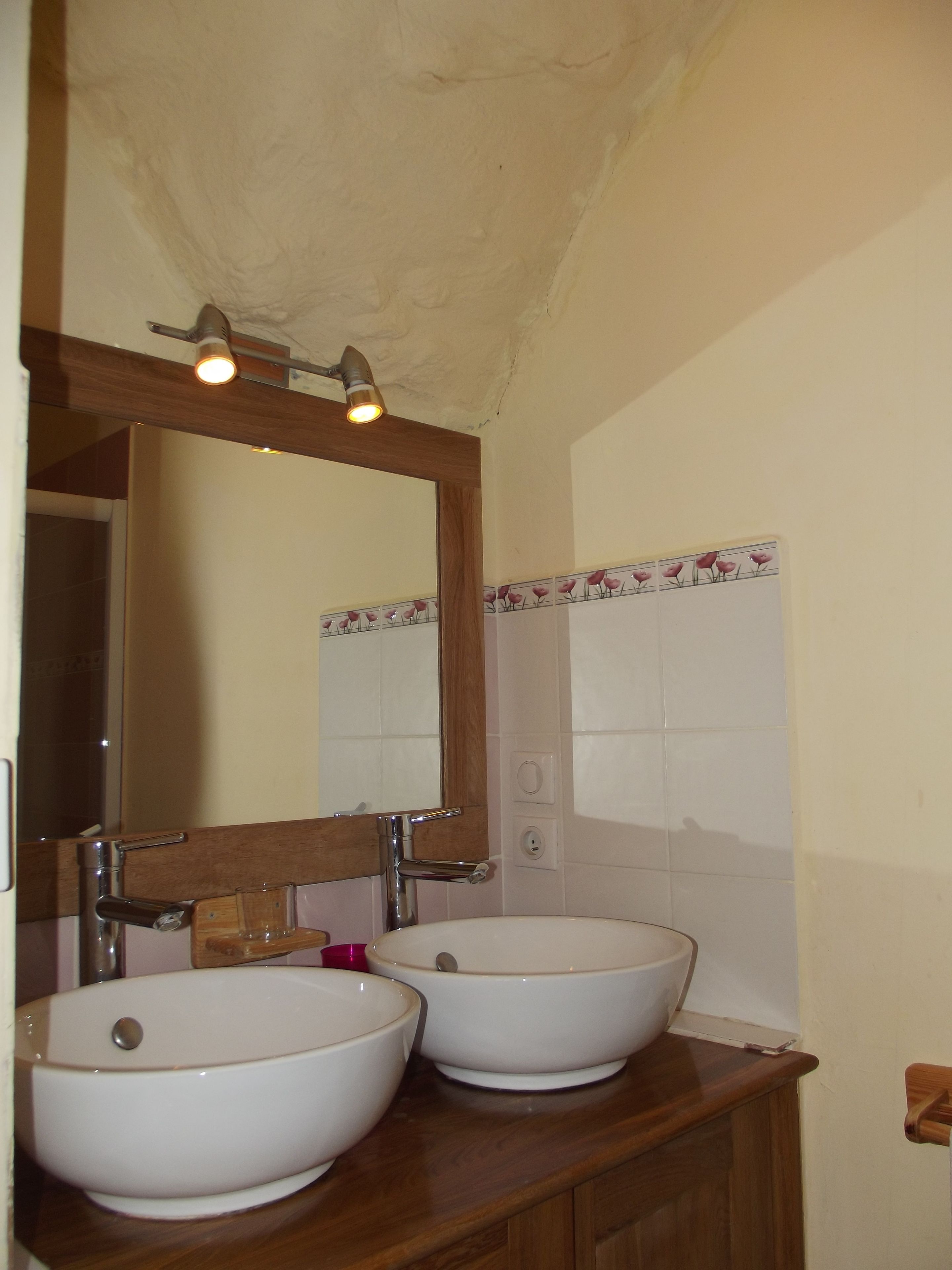 A bathroom with two white sinks, a wooden vanity, a mirror, and a ceiling light fixture.