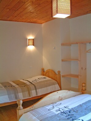 Une chambre avec deux lits en bois, une lampe fixée au mur et une étagère en bois.