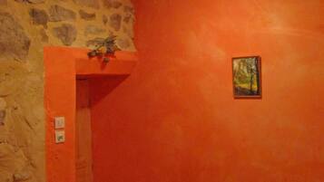 A room with a stone wall, an orange painted wall, a wooden ceiling, a door, and a small framed picture.