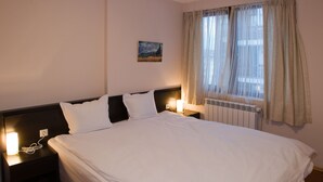A neatly made bed with white linens, a headboard, and two bedside lamps. - Grand Montana (Bansko)