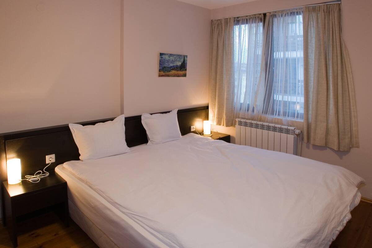 A neatly made bed with white linens, a headboard, and two bedside lamps.