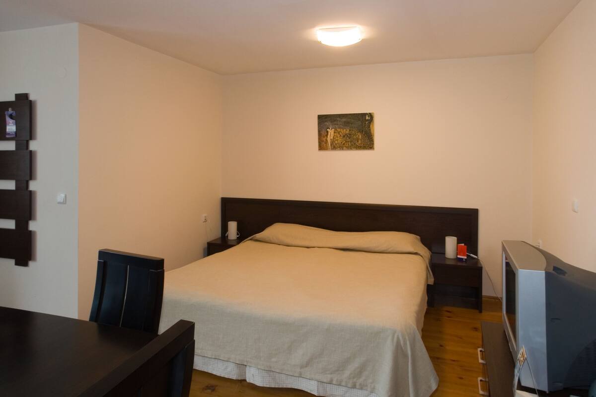 A bedroom with a bed, bedside tables, a TV, and a desk.