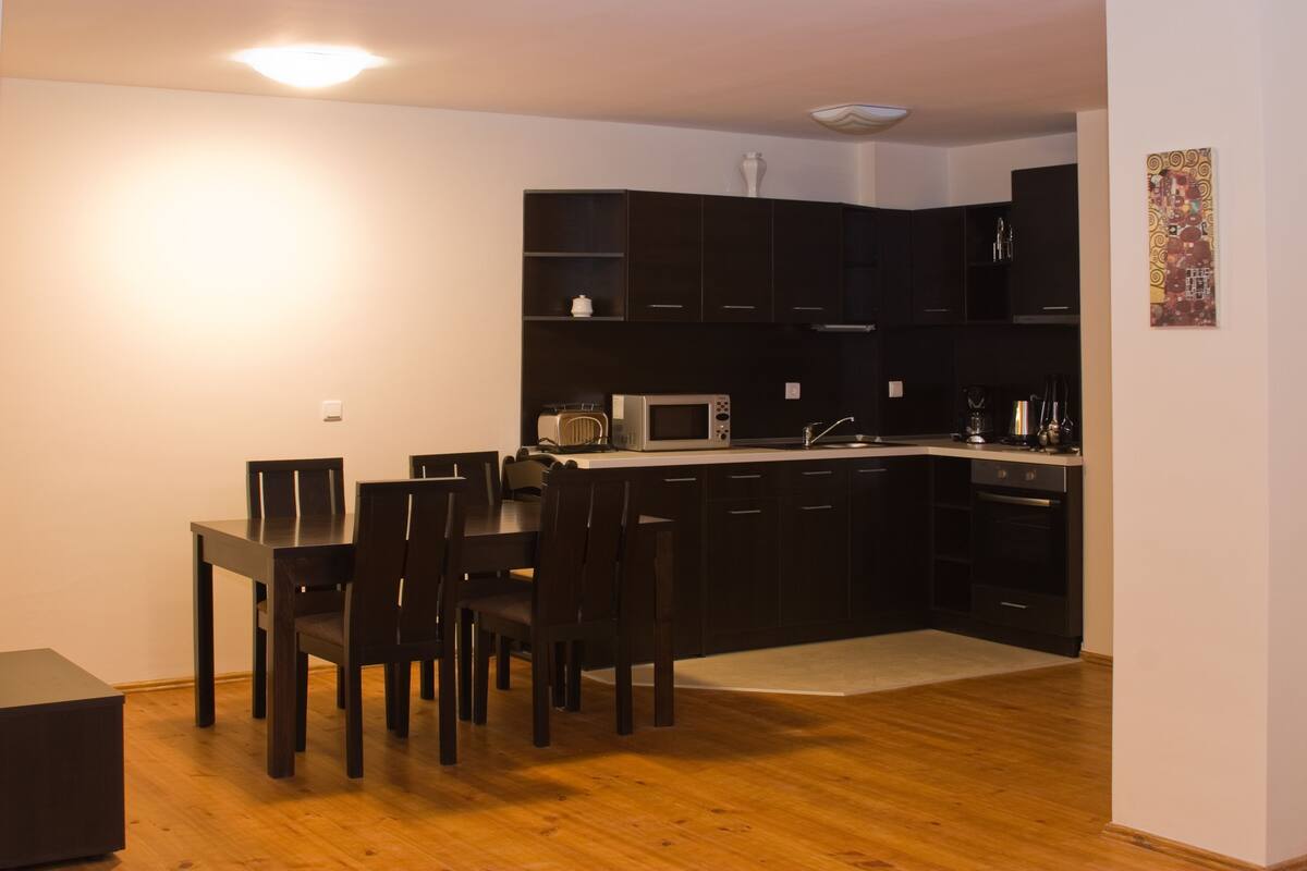 A modern kitchen with dark cabinetry, a dining table with chairs, and a microwave.