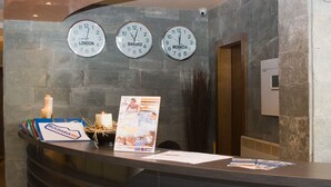 A reception desk with three clocks displaying London, Banská, and Moscow times. - Grand Montana (Bansko)