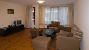 A living room with a sofa, ottomans, a coffee table, and a TV on a wooden cabinet. - Grand Montana (Bansko)