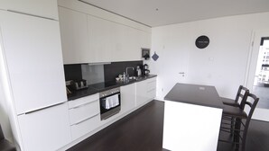 A modern kitchen with white cabinetry, a black countertop, and a built-in oven. There is a coffee maker on the counter and a clock on the wall. - Holiday at Alexanderplatz Apartments (Berlin)