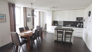 A modern kitchen with white cabinets, a central island with bar stools, and a dining area with a wooden table and chairs. - Holiday at Alexanderplatz Apartments (Berlin)