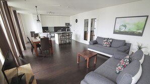 A modern living room with a grey sofa, wooden coffee table, and a dining area with chairs and a kitchen in the background. - Holiday at Alexanderplatz Apartments (Berlin)
