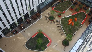 An aerial view of a modern building with multiple floors, outdoor seating areas, and a courtyard with greenery and seating arrangements. - Holiday at Alexanderplatz Apartments (Berlin)
