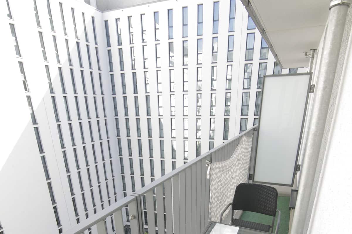 Ein Balkon mit Tisch und zwei Stühlen, der auf einen Innenhof mit Fahrrädern und einem Gebäude im Hintergrund blickt.