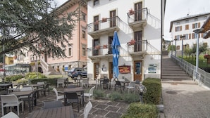 An outdoor cafe with tables and chairs, a staircase leading to a building, and a blue umbrella. - Locanda ai Dogi (Pieve di Cadore)