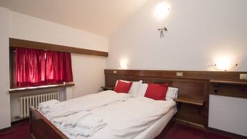 Habitación de hotel con cama, cortinas rojas, cabecera de madera, mesitas de noche e iluminación en la pared.