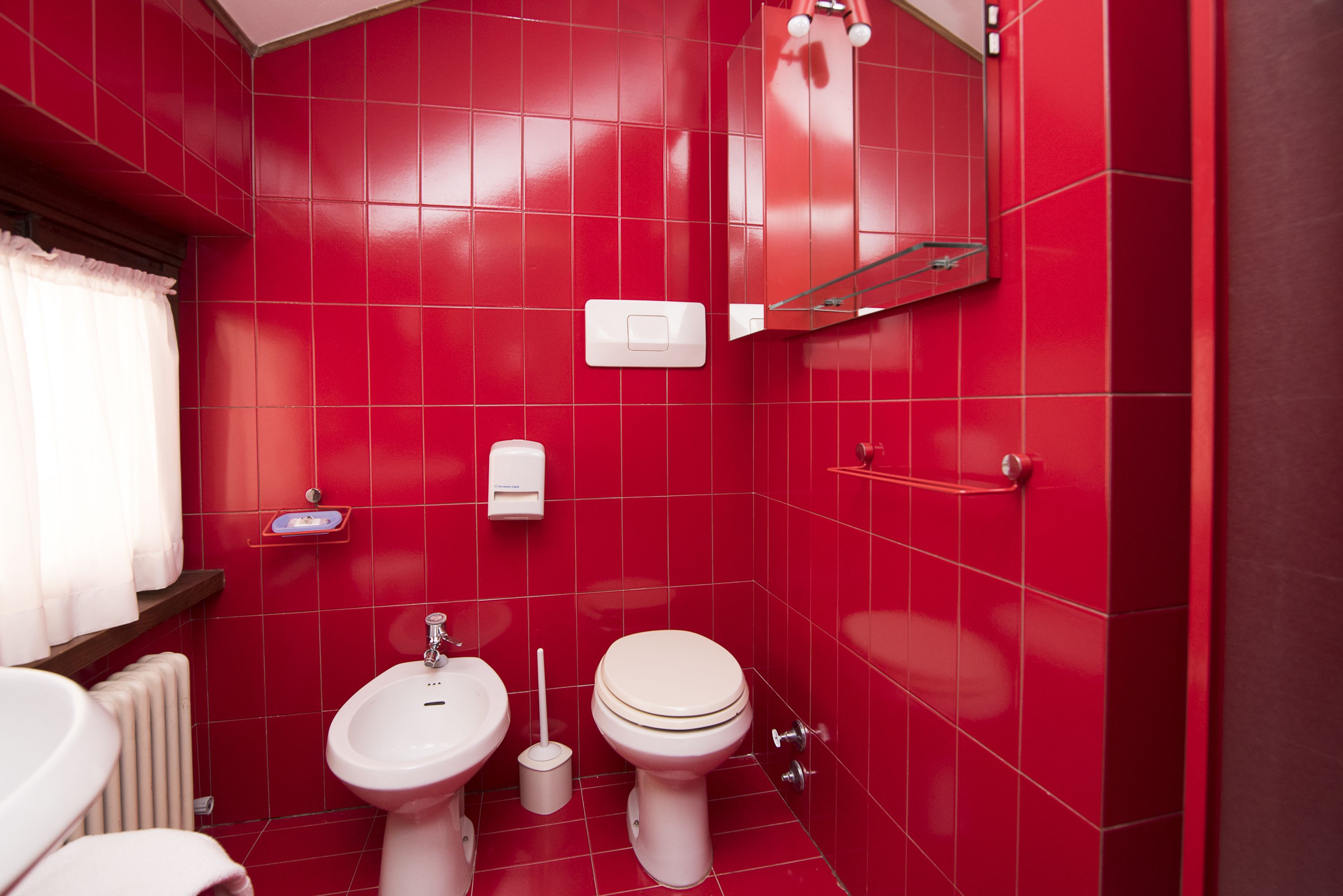Un baño con paredes de azulejos rojos, un inodoro blanco, un lavamanos blanco y un bidé.