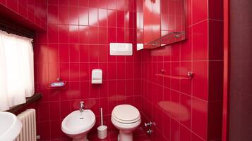 Un baño con paredes de azulejos rojos, un inodoro blanco, un lavamanos blanco y un bidé.