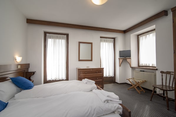 Et hotelværelse med en seng, et kommode, en stol, et fjernsyn og et vindue med gardiner.