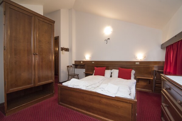 A hotel room with a large wooden wardrobe, a bed with white linens, two bedside tables, and a red curtain. - Locanda ai Dogi (Pieve di Cadore)