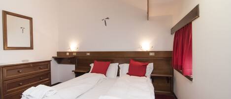Habitación de hotel con una cama grande, un aparador de madera, un espejo y una ventana con cortinas rojas.