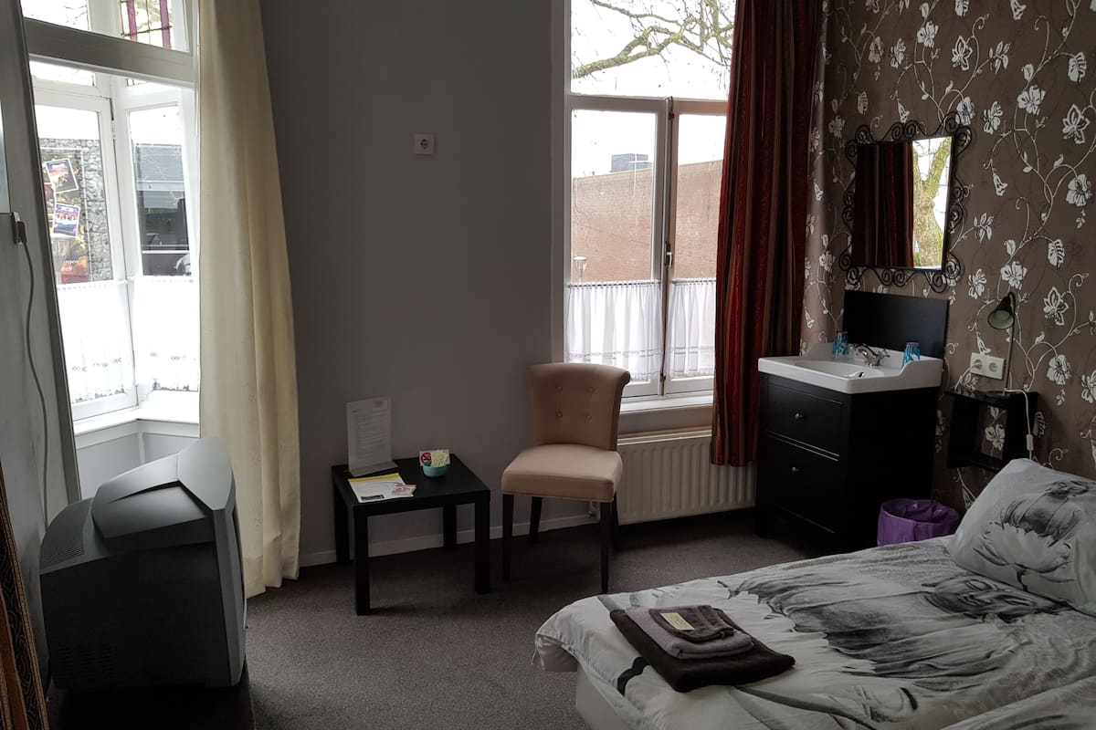 A hotel room with a bed, a chair, a desk, a dresser, a mirror, and a window with curtains.