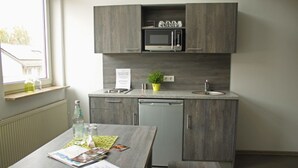 A compact kitchen with a microwave, sink, and dishwasher. There is a window with a view of buildings outside, and a table with a plant and some items on it. - Komfort Apartments am Marktplatz (Bexbach)