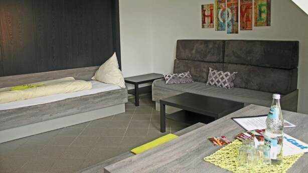 A modern room with a bed, a sofa, a coffee table, and a wall with colorful artwork. - Komfort Apartments am Marktplatz (Bexbach)