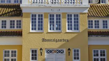 Un bâtiment jaune dont la façade porte l’inscription « Admiralgaarden », avec une porte blanche et de nombreuses fenêtres.