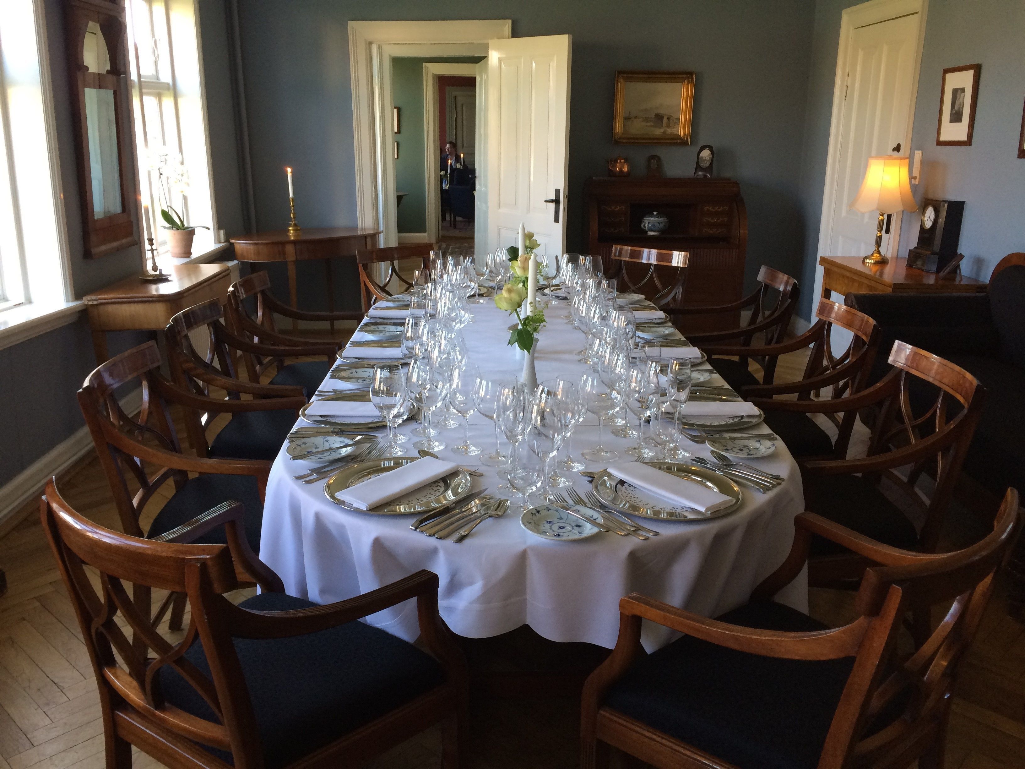 A formal dining room with a long table set for a meal, surrounded by wooden chairs.