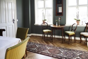 Ein Zimmer mit Esstisch, zwei Stühlen, einem gemusterten Teppich und Blumentöpfen an einem Fenster.