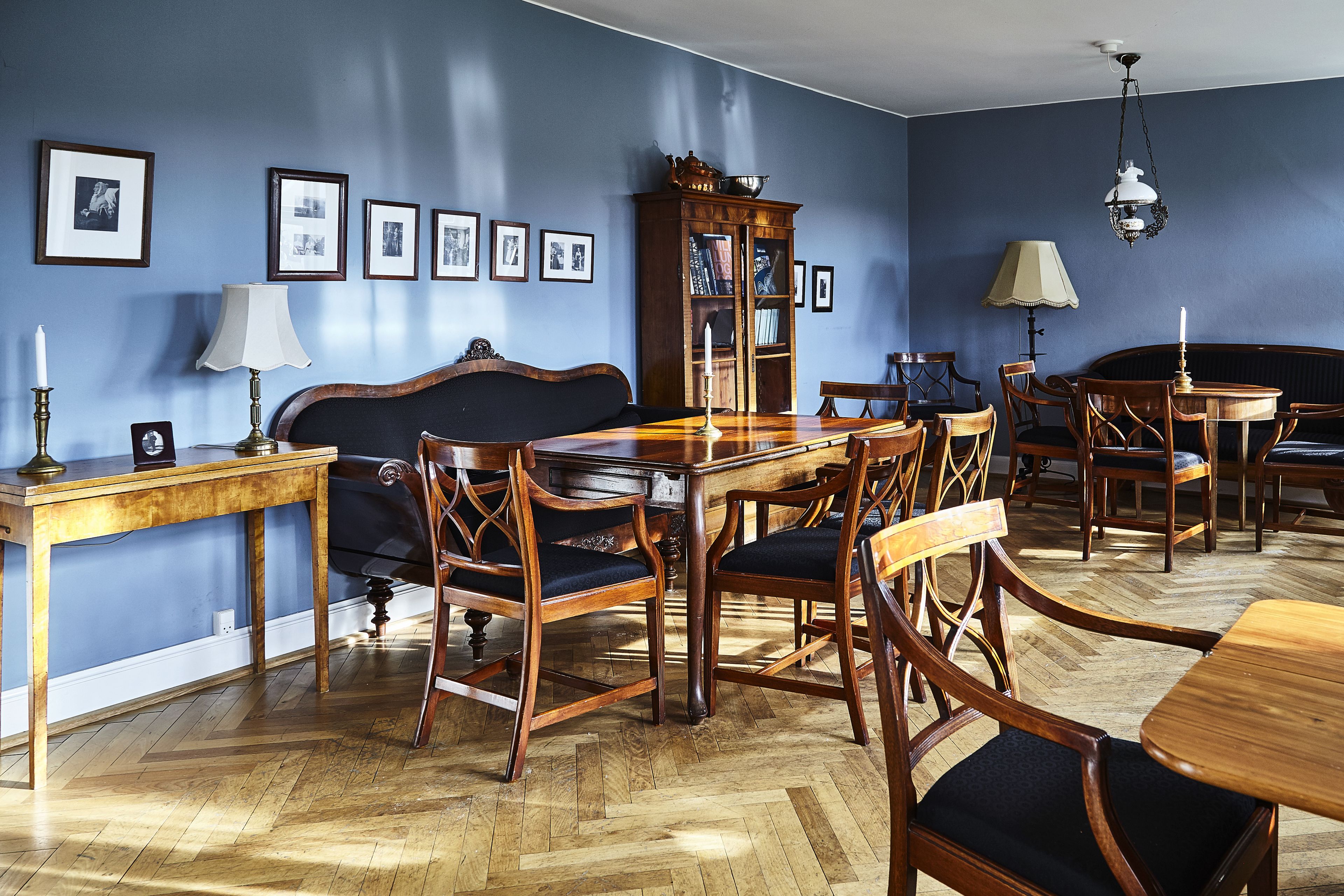 Un comedor con una mesa de madera, sillas, una estantería y cuadros en la pared.