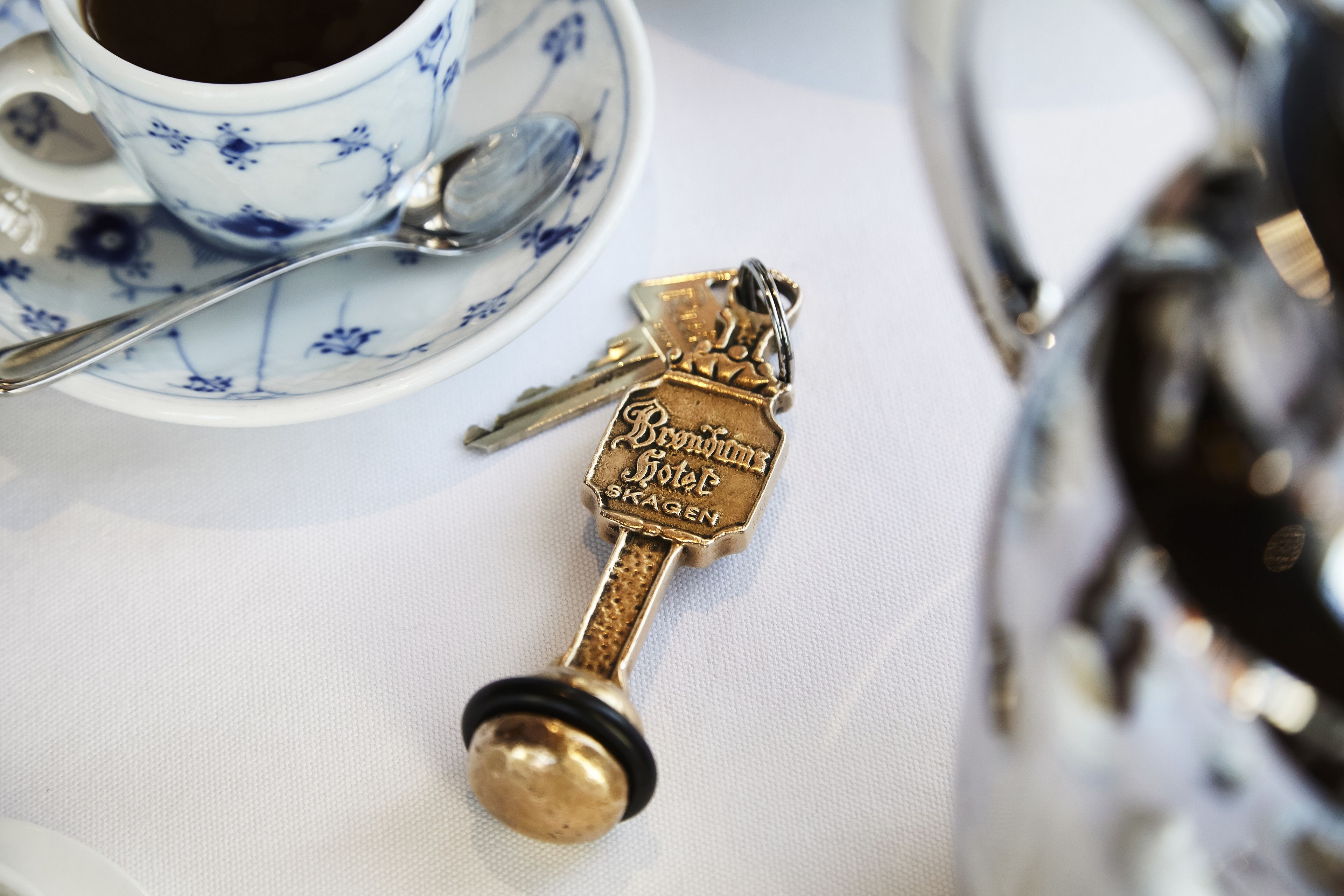A vintage key, a spoon, and a cup with floral patterns on a table.