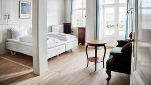 A hotel room with a bed, a small round table, a chair, a TV, and a window with curtains. - Brøndums Hotel (Skagen)