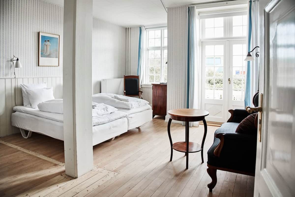 Et hotelværelse med seng, et rundt bord, en stol, et fjernsyn og et vindue med gardiner.