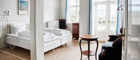 A hotel room with a bed, a small round table, a chair, a TV, and a window with curtains.