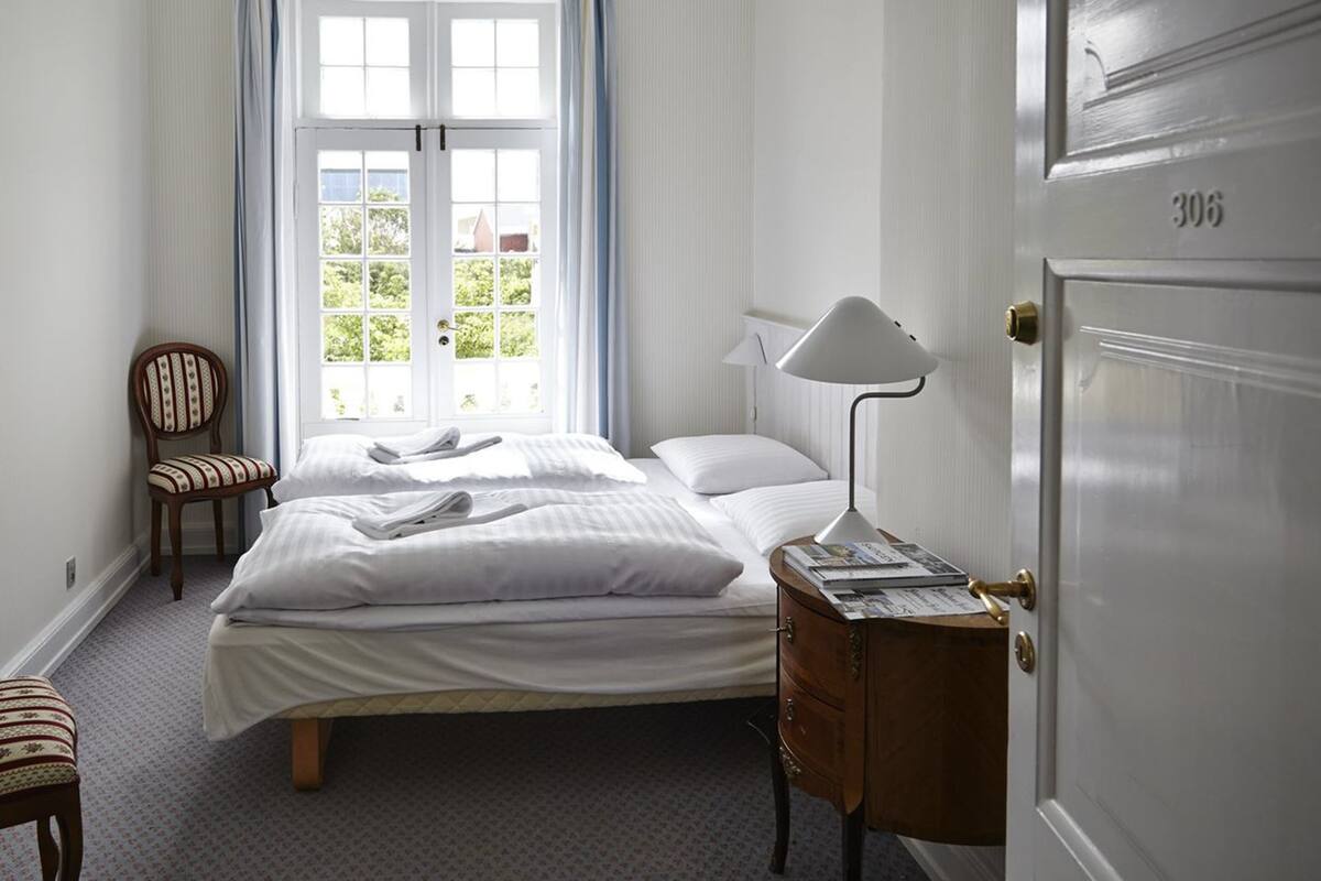 Et pænt møbleret soveværelse med en dobbeltseng, en stol, et sengebord med lampe og en dør med et nummer.