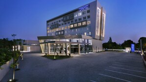Ett modernt hotell med en framträdande skylt med texten ”ASTON”, en överbyggd entré och en rymlig parkeringsplats.