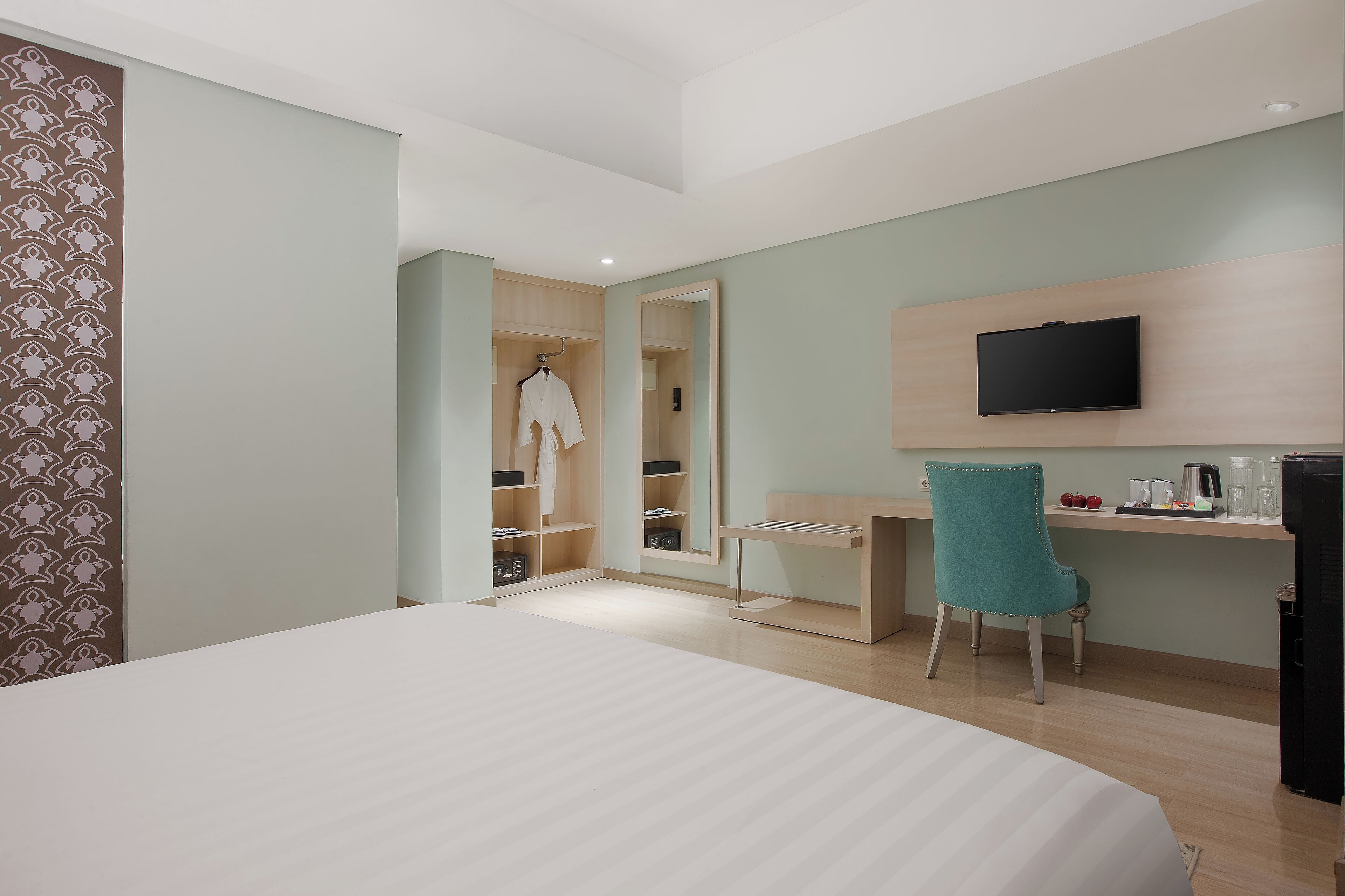 A hotel room with a bed, a desk, a chair, a TV, and a wardrobe.