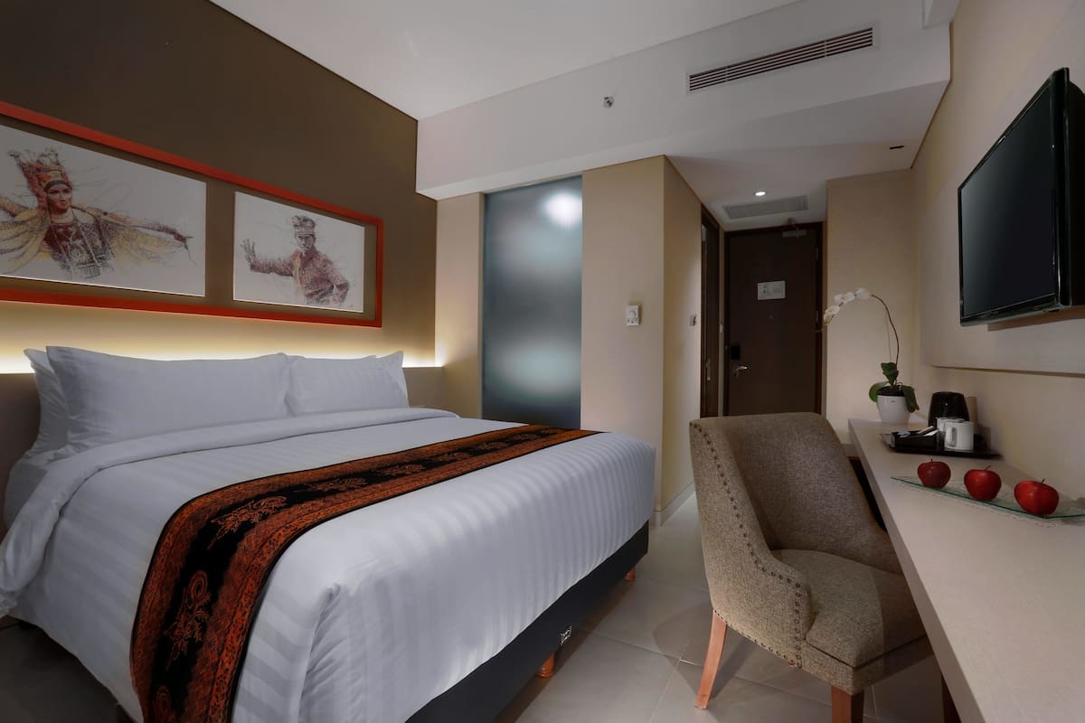 A hotel room with a bed, a desk with a chair, a TV, and artwork on the wall.