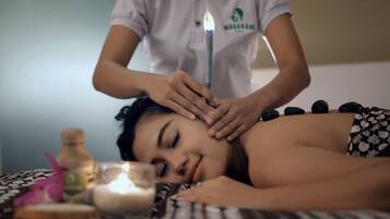 A person receiving a massage with a lit candle in a room with a bed, a bottle, and a glass.