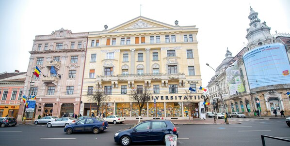 A university building with classical architecture, a central entrance, and a large banner on the right side.