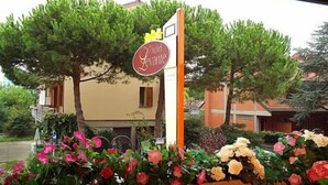 A hotel entrance with a sign reading "Hotel Levante," surrounded by flowering plants and trees. - Hotel Levante (Cervia)