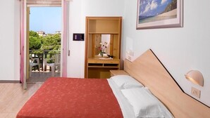 Habitación de hotel con cama, mesita de noche y espejo. Se ve una puerta que da a un espacio exterior con sillas y una mesa.