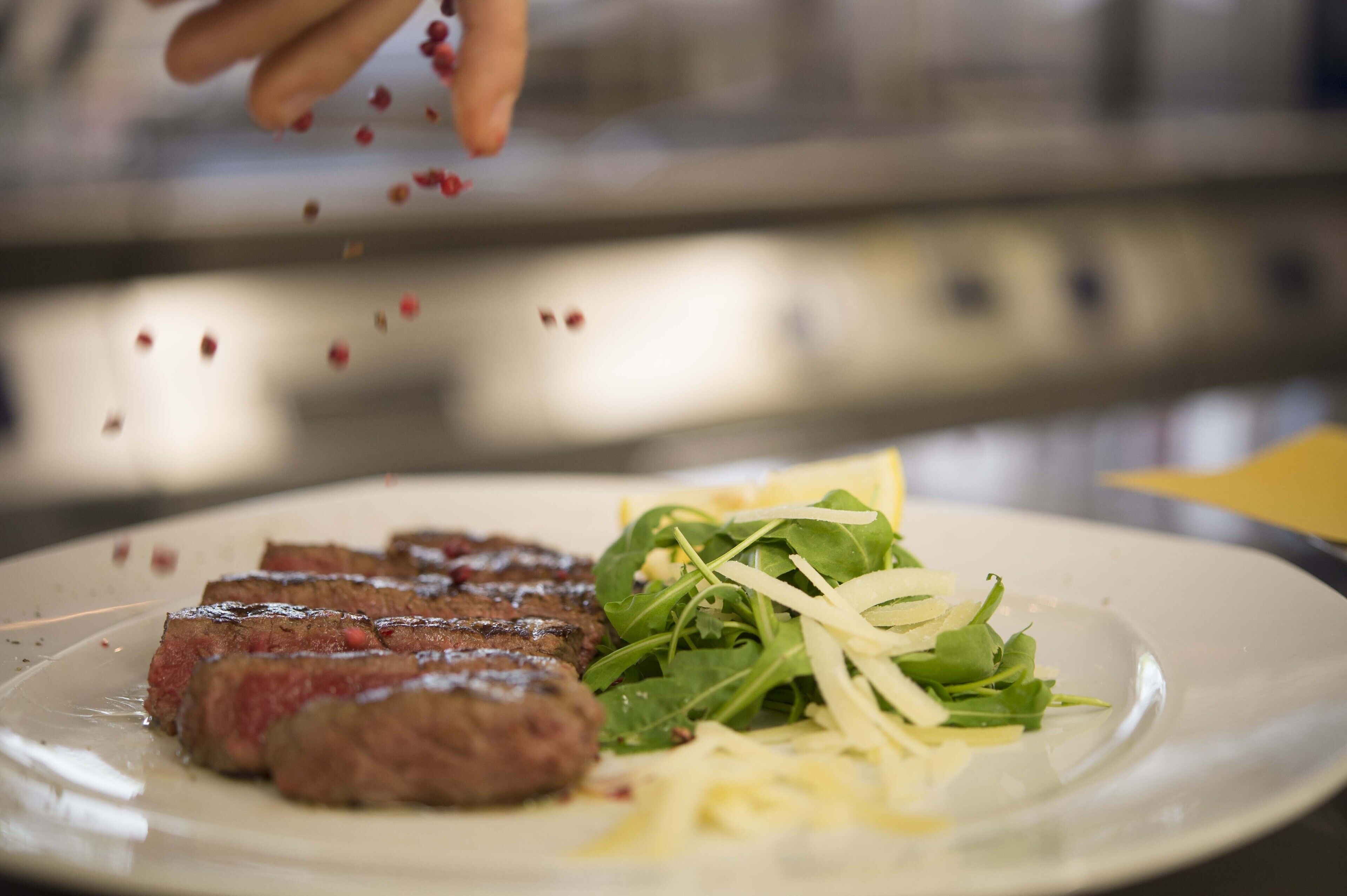 Une assiette avec de la viande tranchée et des légumes verts, peut-être un steak accompagné d’une salade de roquette et de copeaux de fromage.