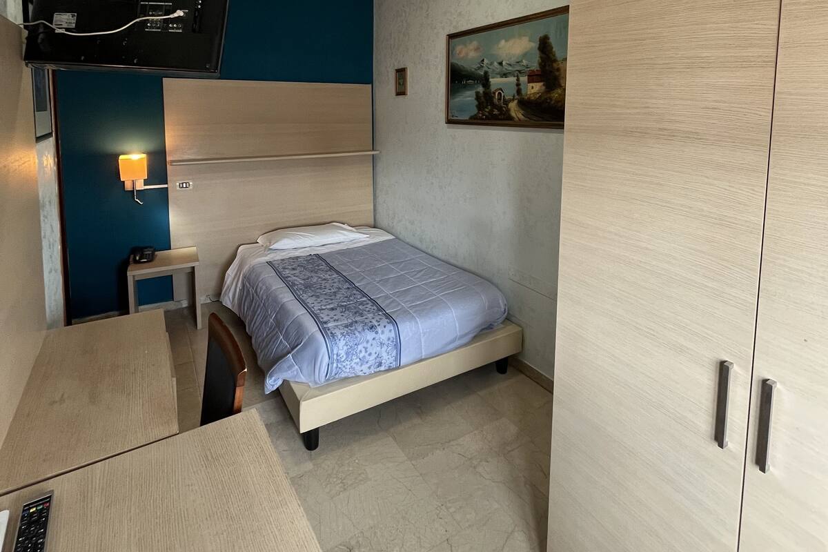 A compact hotel room with a bunk bed, a desk with a computer, a wardrobe, and a painting on the wall.
