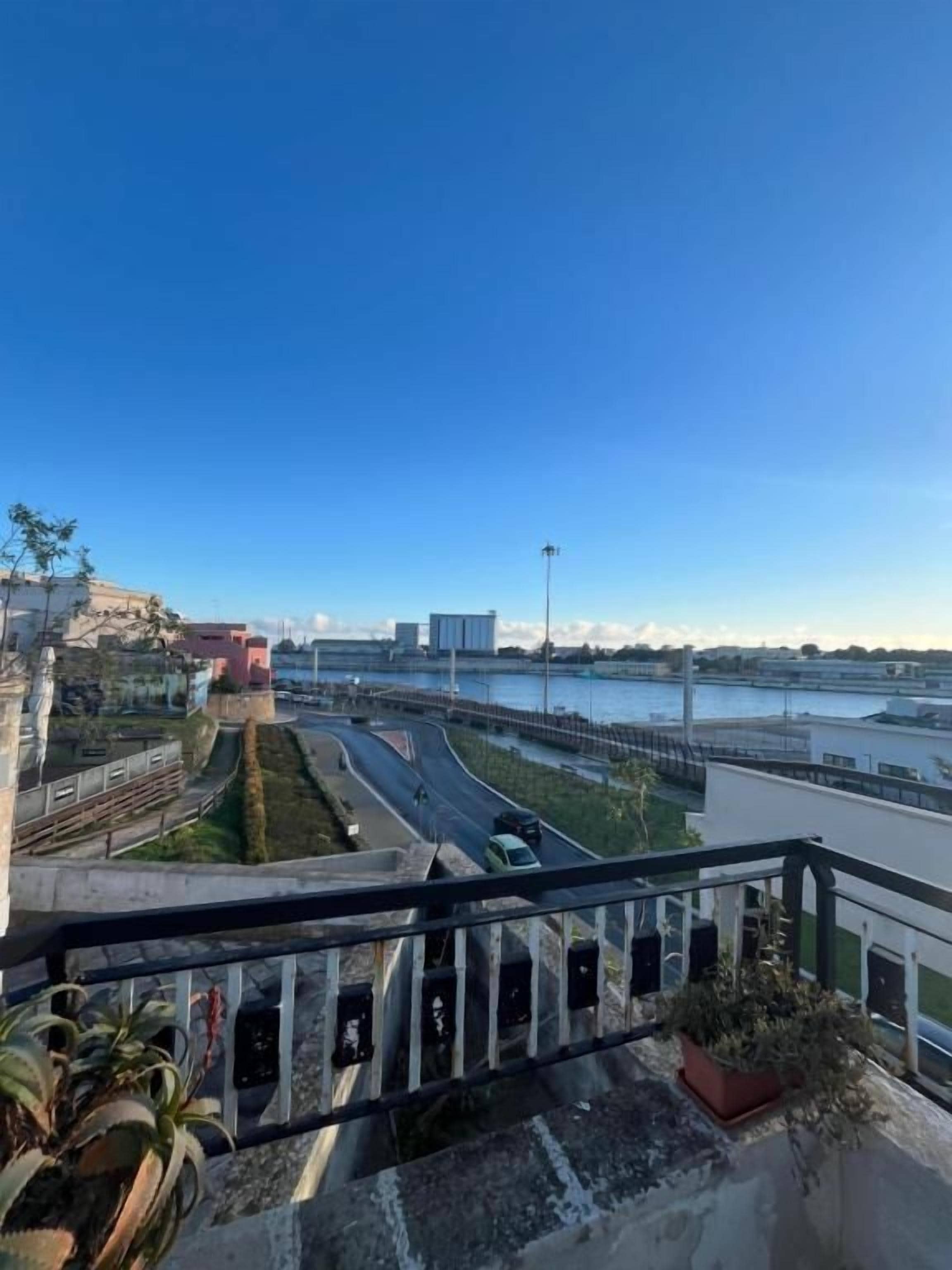 Blick von einem Balkon auf einen Fluss mit einer Brücke, einer Straße und etwas Grün.