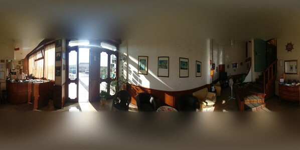 Een panoramisch uitzicht op een kamer met een houten bureau, een bank en een trap.