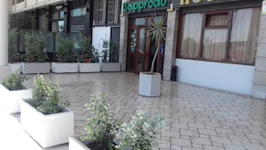 Een buitenruimte met potplanten en een gebouwde ingang met een bord waarop 'Cappuccino' staat.