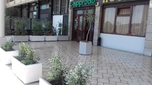 An outdoor area with potted plants and a building entrance with a sign that reads "Cappuccino". - Hotel L'Approdo (Brindisi)