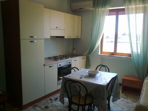 A compact kitchen with a dining table, chairs, and a window with curtains. - Hotel L'Approdo (Brindisi)