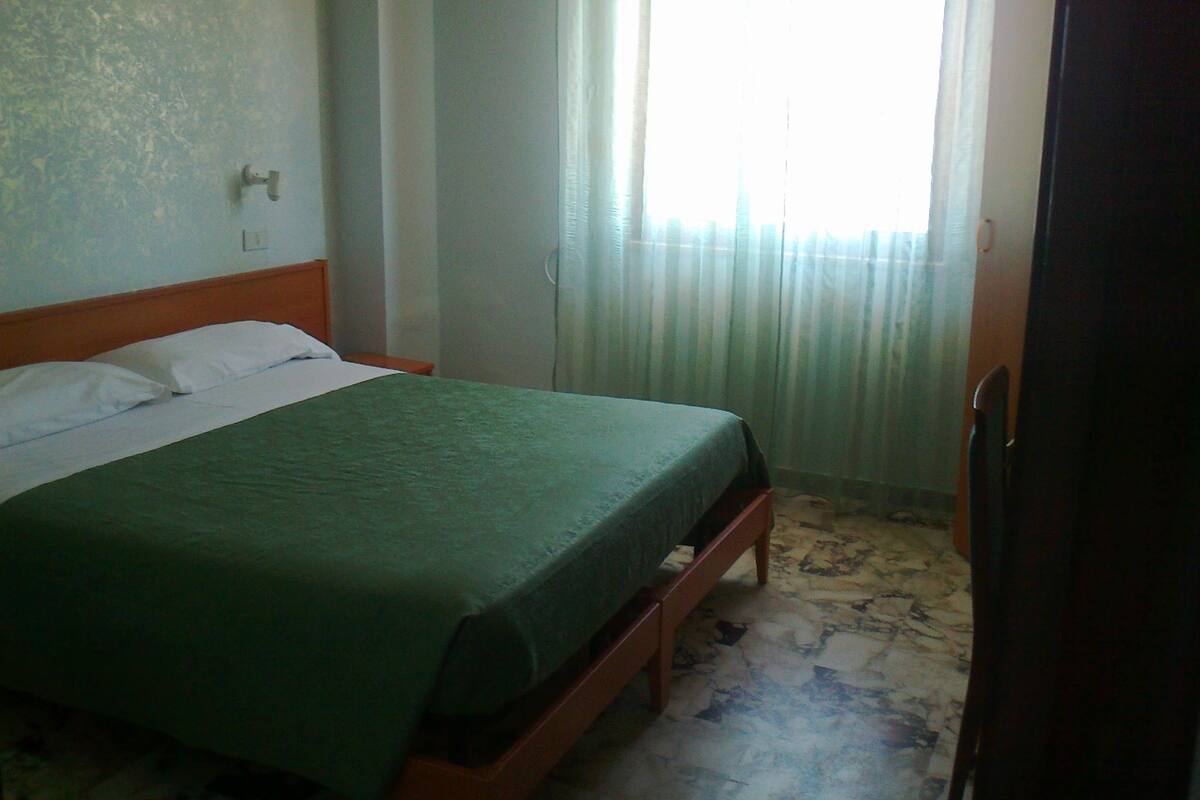 A single bed with a wooden frame and a green bedspread in a room with a patterned floor.
