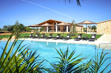 Una piscina al aire libre, sombrillas, sillones reclinables de piscina