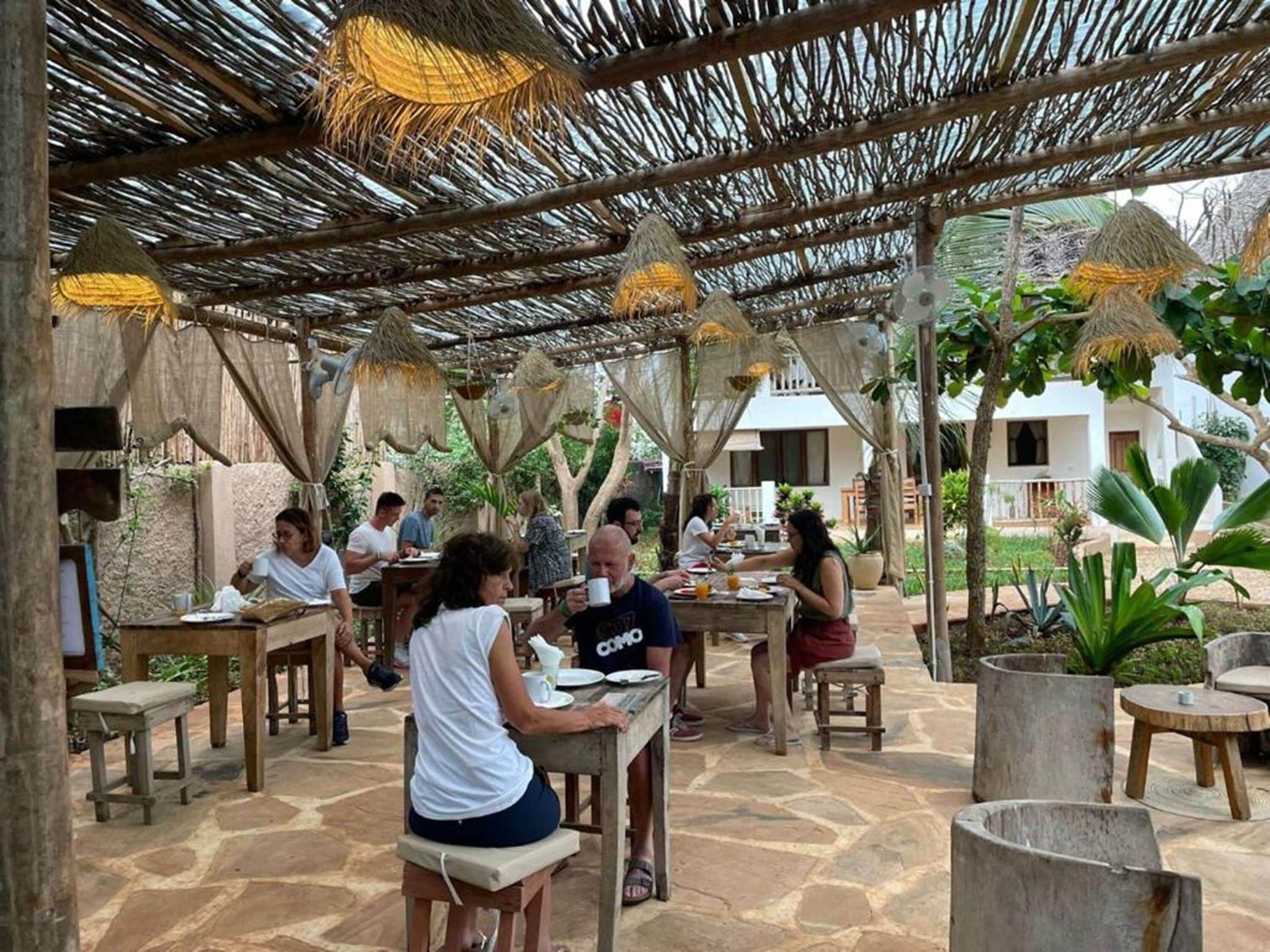 Een terras met rieten dak en stenen vloer, met houten tafels en banken.